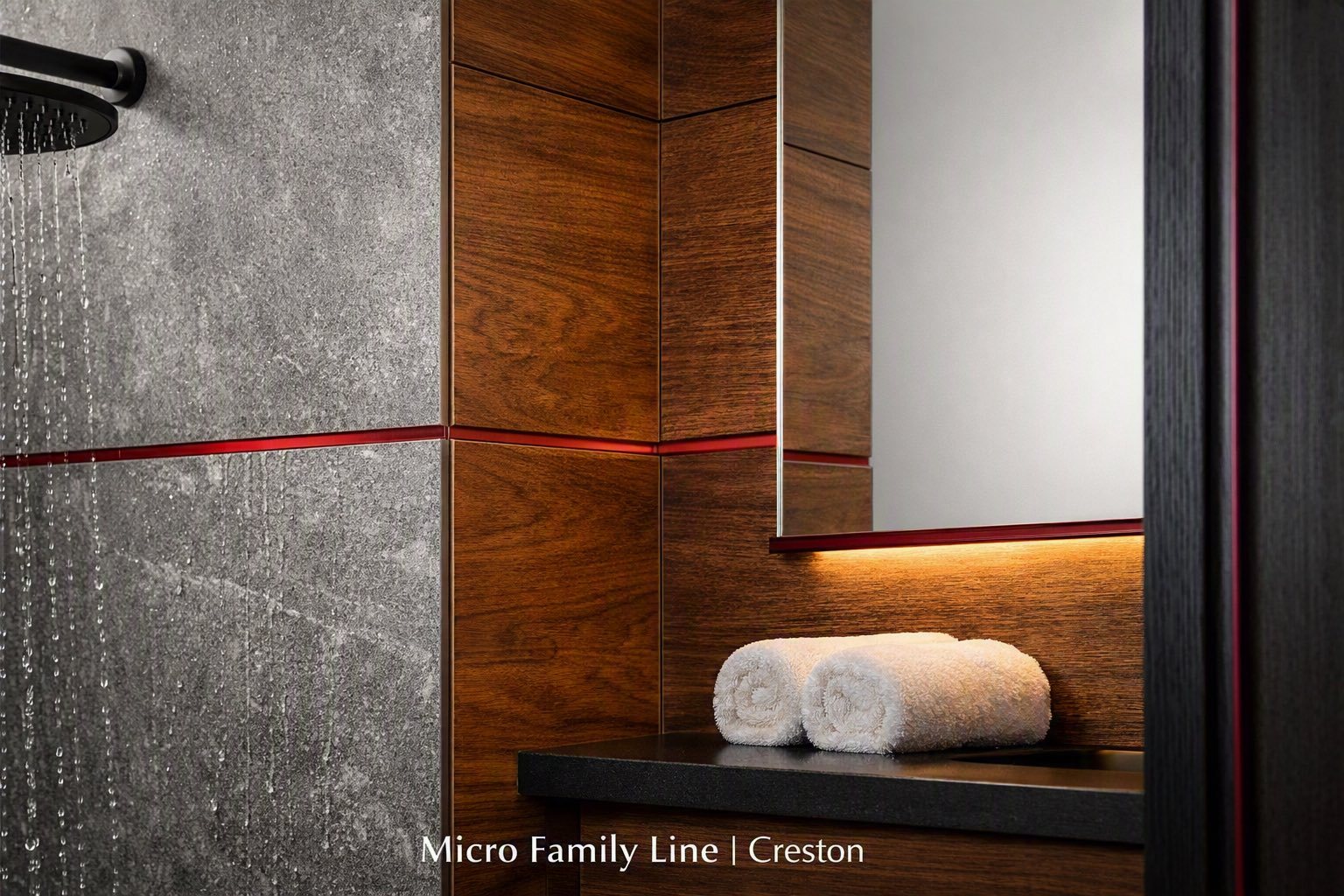 Bathroom detail with grey stone shower wall and walnut panelling, a burgundy line running through both materials and along the mirror shelf, with rolled white towels. Image captioned Micro Family Line, Creston.
